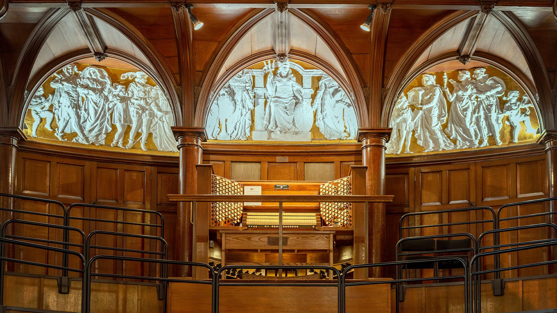 Wooden panelled wall with white figures in arches above and organ in the centre on a raised plinth.