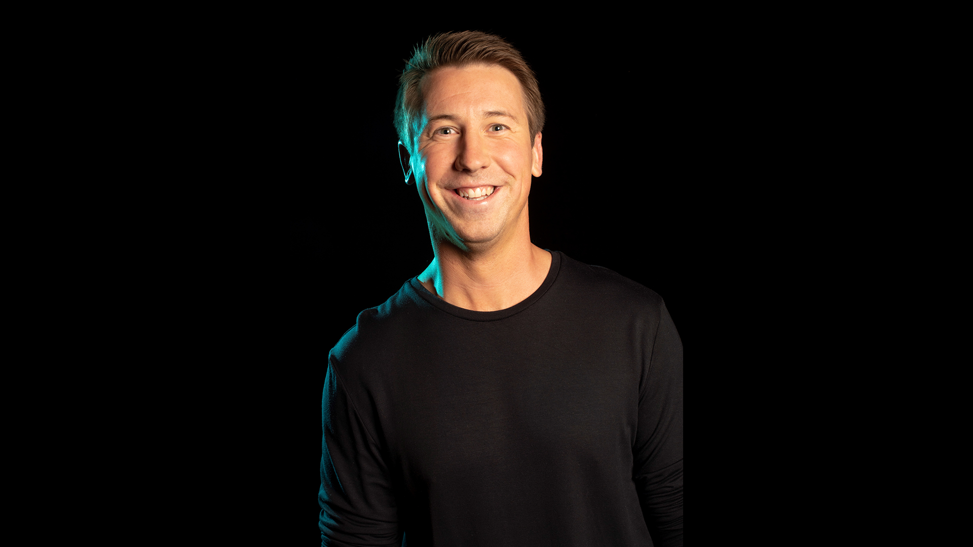 A man smiles in front of a black background