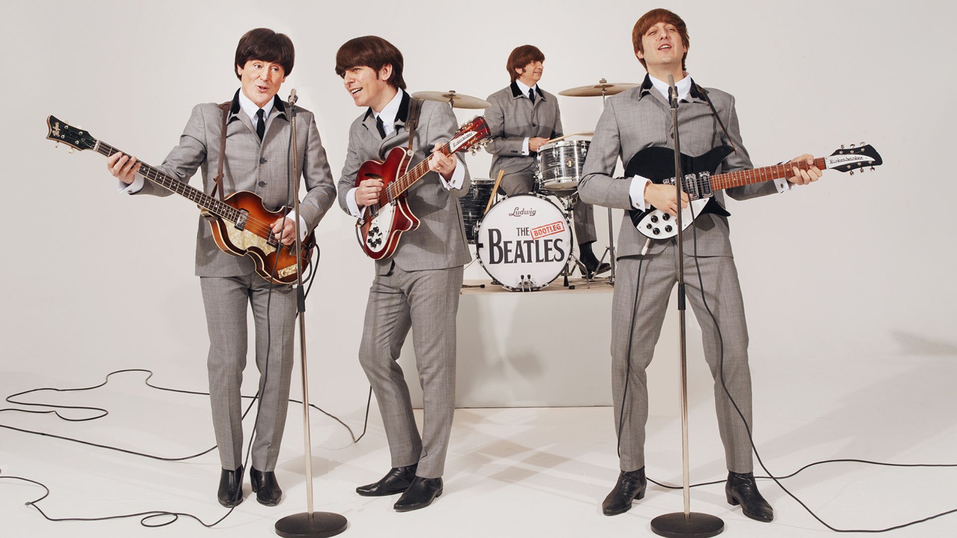 Four men perform as the Beatles with grey suits and bowl cuts. 