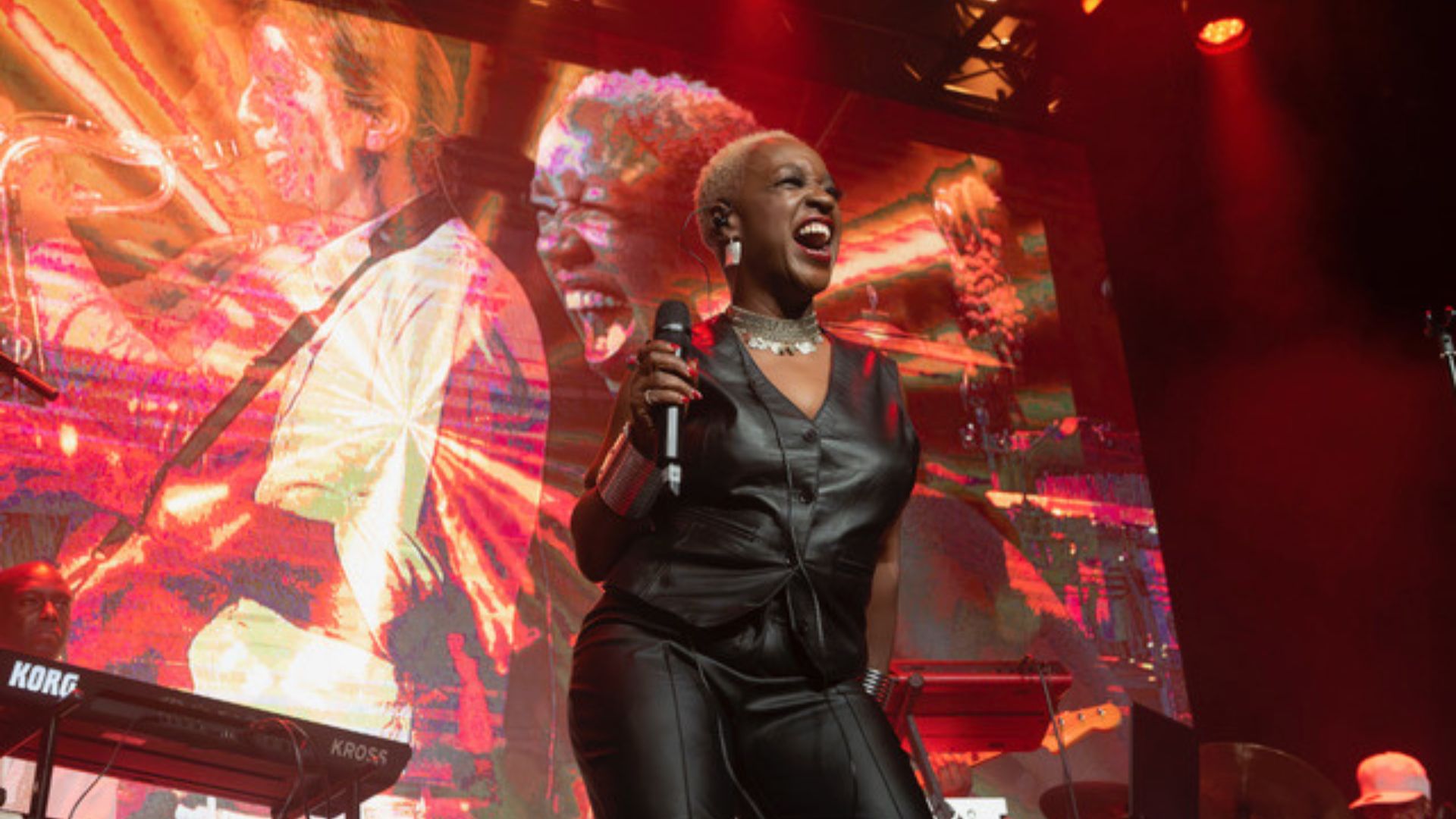 Female singer in Black Leather trousers and waistcoat with digital screen of her singing in the background