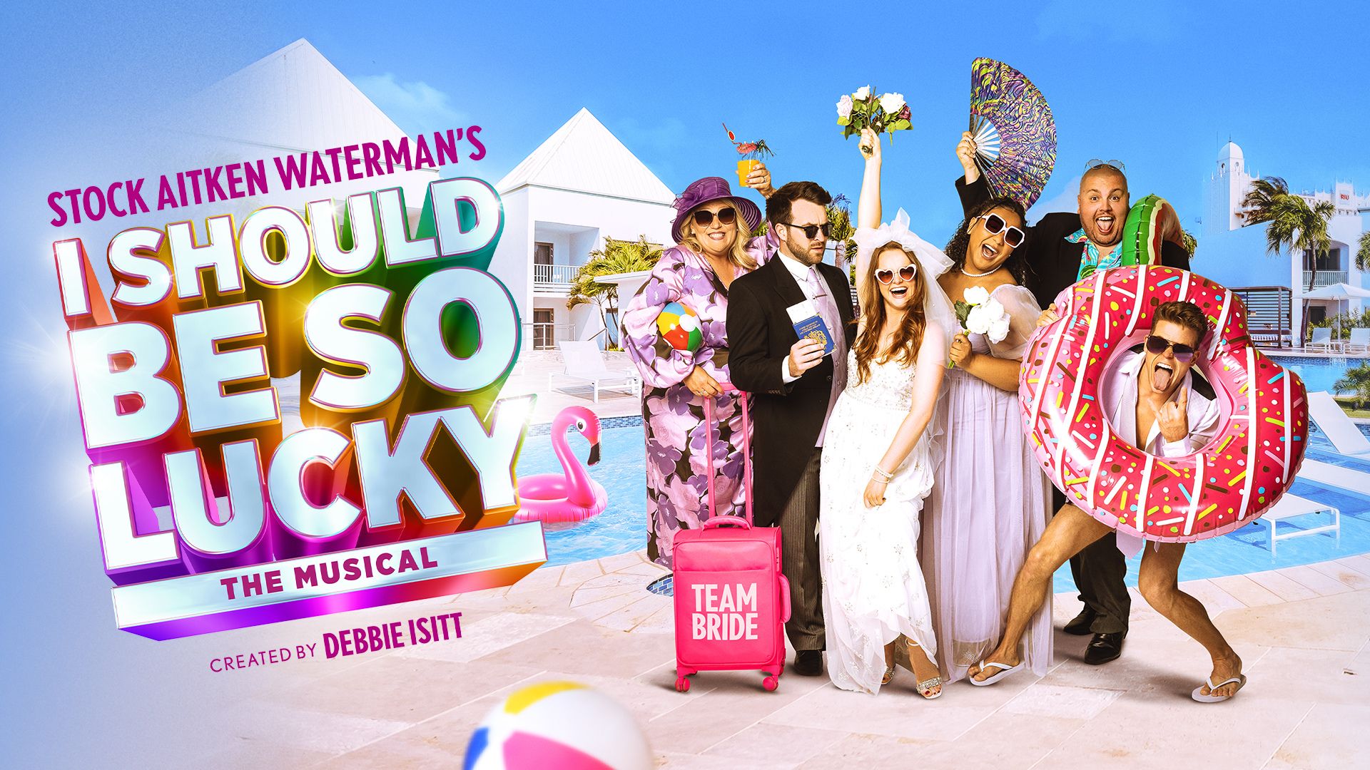 A wedding party pose in front of a hotel swimming pool with suitcases, cocktails and pool inflatables 